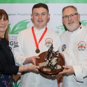 Junior Chef of Wales winner Sam Everton receives the dragon trophy from Minister for Rural Affairs Lesley Griffiths and CAW president Arwyn Watkins, OBE.